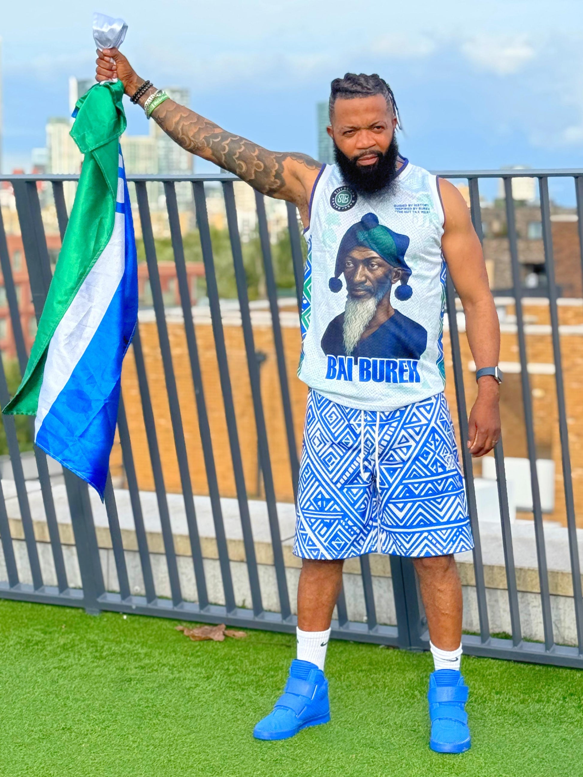 Person holding a flag with a scenic background with a sierra Leone Hero printed on the sleeveless 