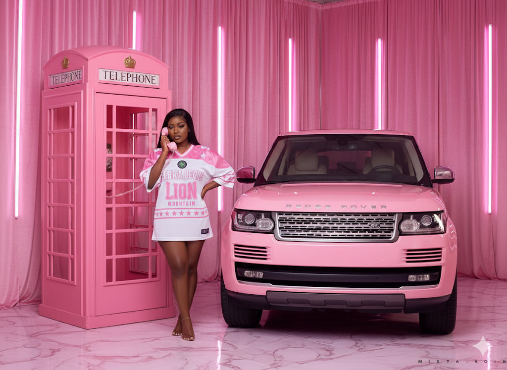 Woman in a pink and white outfit standing next to a pink Range Rover in a pink-themed setting.