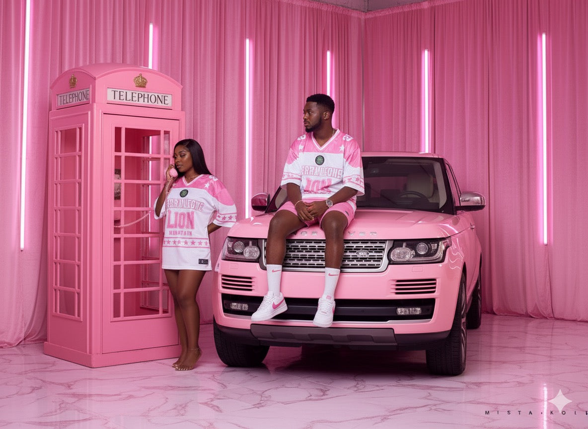 Two people in matching pink outfits sitting on a pink Range Rover with a pink telephone booth in the background.