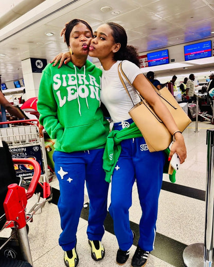 Two people in matching outfits with 'Sierra Leone' embroidery patch at an airport.