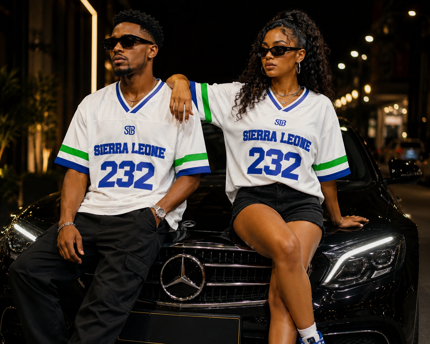 Two models wearing matching white 'SIERRA LEONE 232' jerseys with blue and green accents, posing on a black Mercedes-Benz car at night.