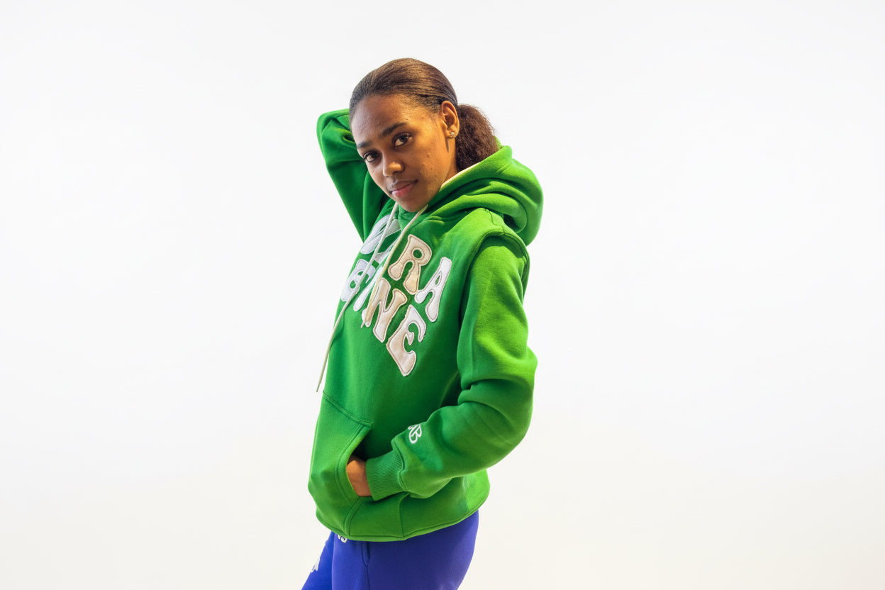 Person wearing a green hoodie with Sierra Leone patch embroidery and blue pants. Side view 