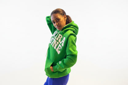 Person wearing a green hoodie with Sierra Leone patch embroidery and blue pants. Side view 