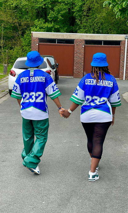 Two people wearing matching blue and green outfits with 'King Sannoh' and 'Queen Sannoh' text, walking hand in hand on a street.