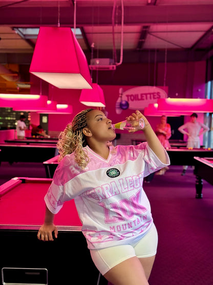 Woman in a pink and white sports jersey standing in a pink-themed pool hall.