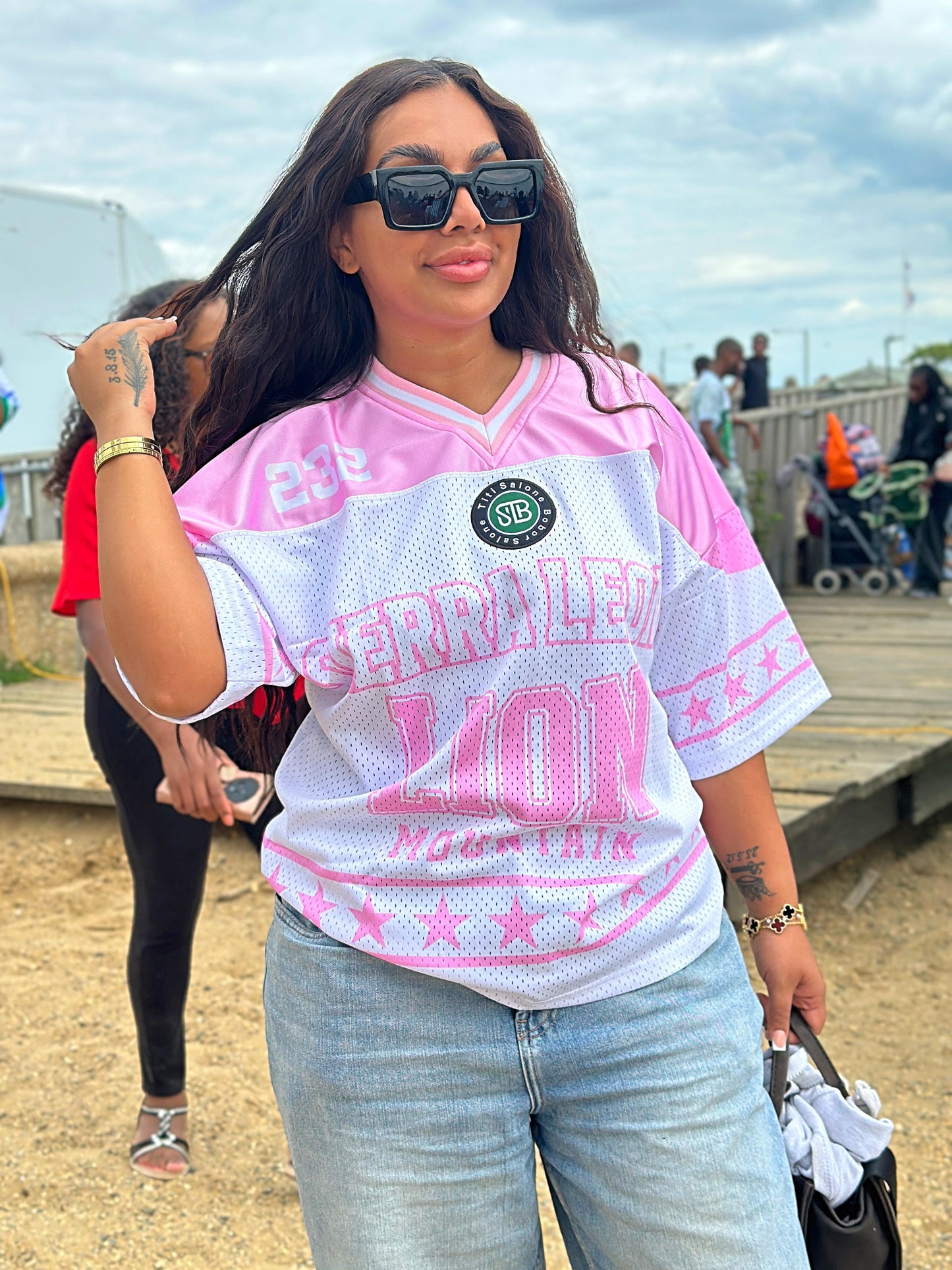 Woman wearing a pink and white sports jersey with text, standing outdoors.